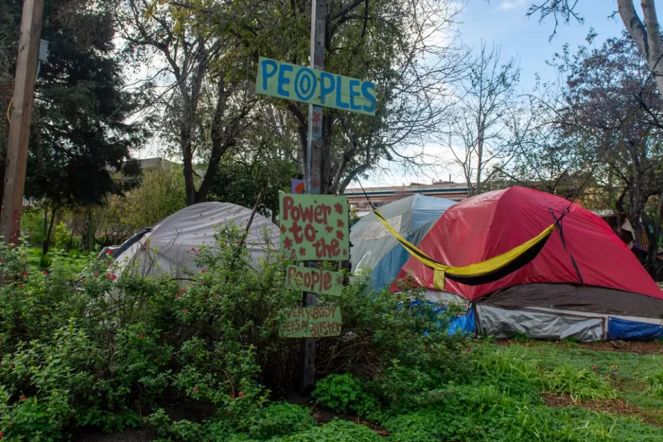 Tents fpor people experiencing homelessness are surrounded by signs that impart messages of resistance to change.